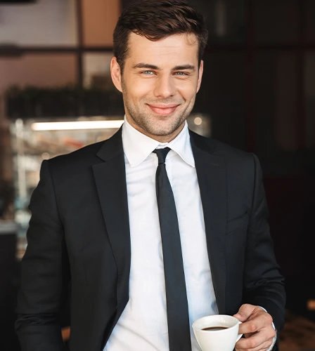 Smiling young businessman in a black suit holding a white cup of coffee, representing focus and steady daily energy.